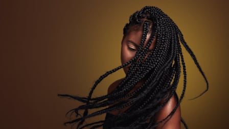 Woman with long, intricately braided hair partially covering her face, against a warm-toned gradient background